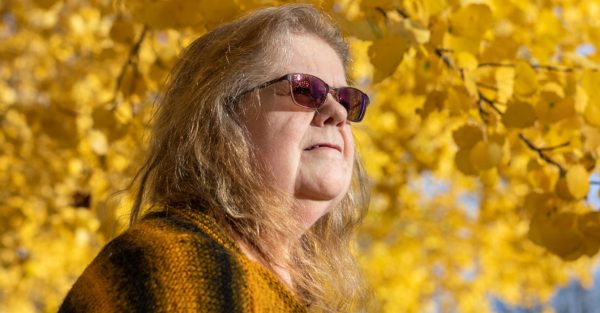 Bild på en kvinnas ansikte mot en höstig bakgrund, innehållandes gula löv i ett träd. Hon bär solglasögon.